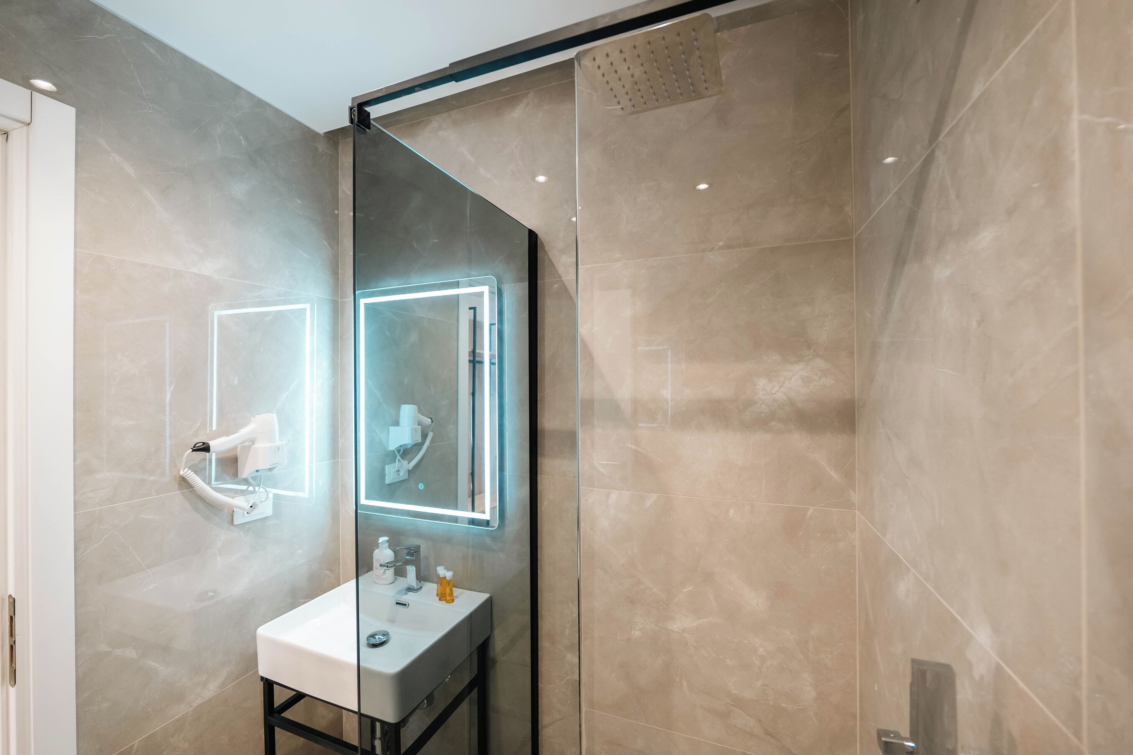 A modern bathroom with a glass shower enclosure, a white sink, and a mirror with integrated lighting.
