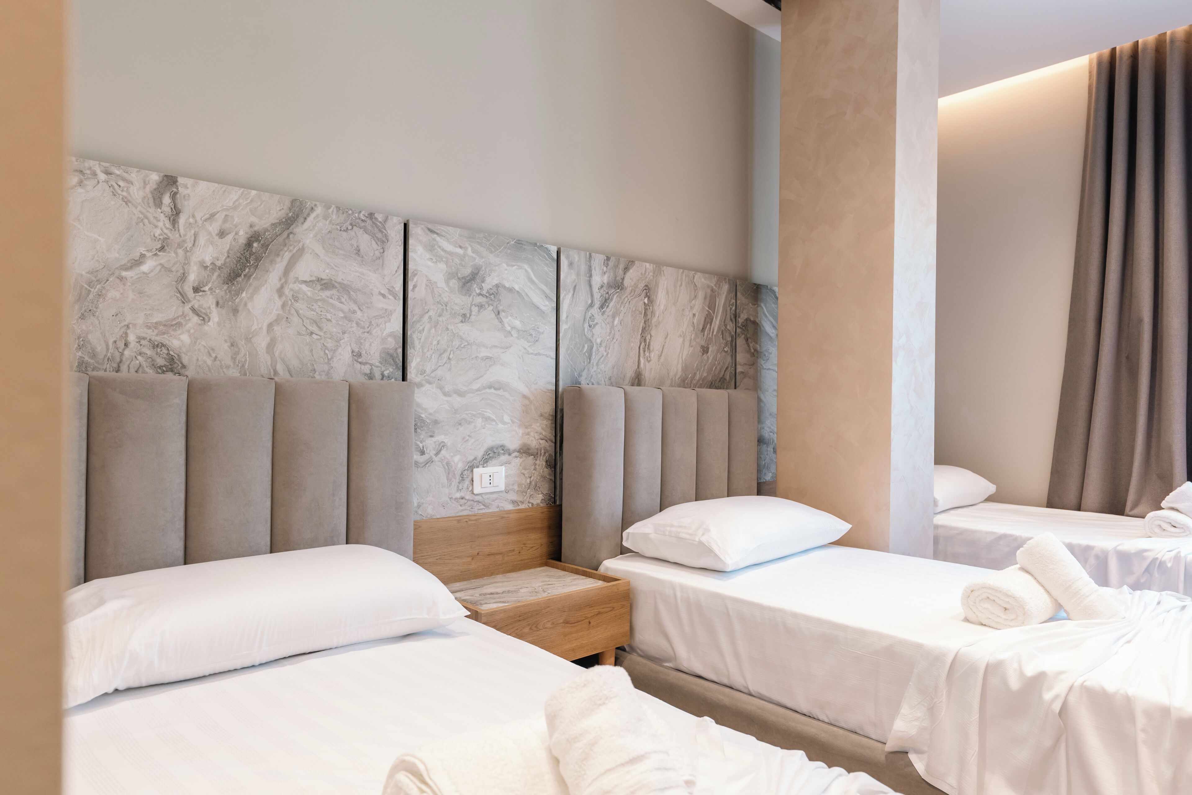 A hotel room with two beds, a marble headboard, and a wooden nightstand.