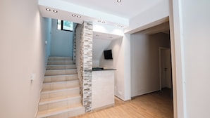 Un intérieur moderne avec un escalier, un coin cuisine intégré et un téléviseur à écran plat fixé au mur.
