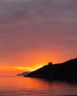 A sunset over a coastal landscape with a silhouette of a hill and a structure on it. - CasadiCampo II (Scauri)