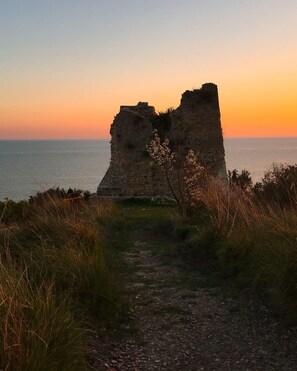 A historical stone structure with a pathway leading to it, overlooking a body of water.