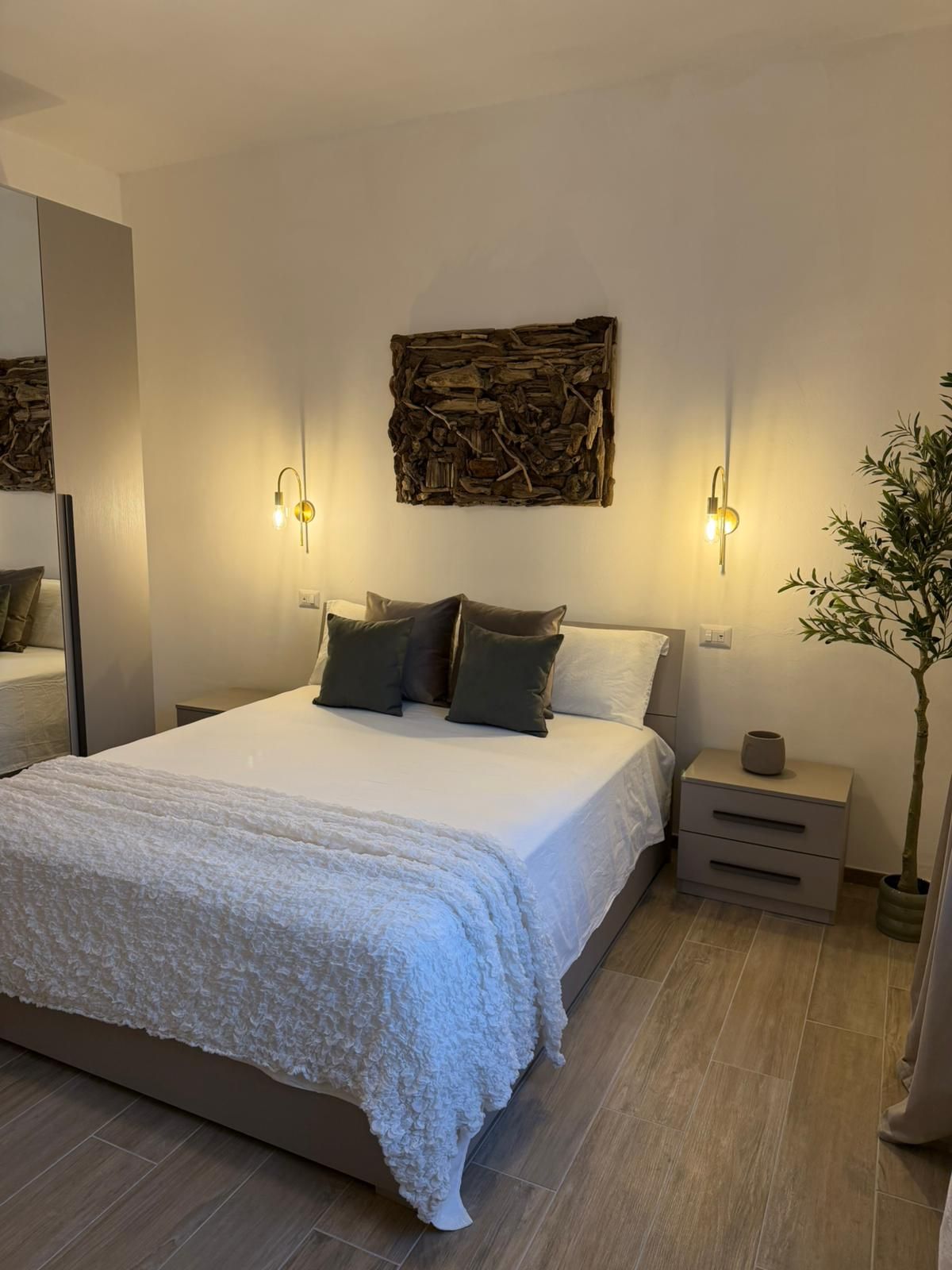 Een slaapkamer met een groot bed, twee nachtkastjes, een wandlamp en een kamerplant.