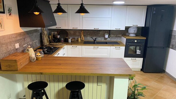 A modern kitchen with white cabinets, a wooden countertop, black bar stools, and a black refrigerator. - Mary House (Scauri)