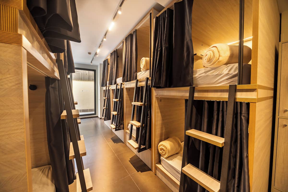 Un couloir d’hôtel avec des lits superposés, des têtes de lit en bois et des rideaux noirs.