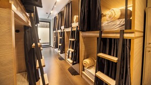 Un couloir d’hôtel avec des lits superposés, des têtes de lit en bois et des rideaux noirs.