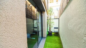Une petite cour intérieure recouverte d’un gazon synthétique, avec un pot de fleurs et une porte vitrée donnant sur une pièce.