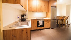 Une cuisine moderne avec des armoires en bois, un évier en acier inoxydable, un four encastré et un réfrigérateur. Il y a deux chaises en bois près du comptoir de la cuisine.