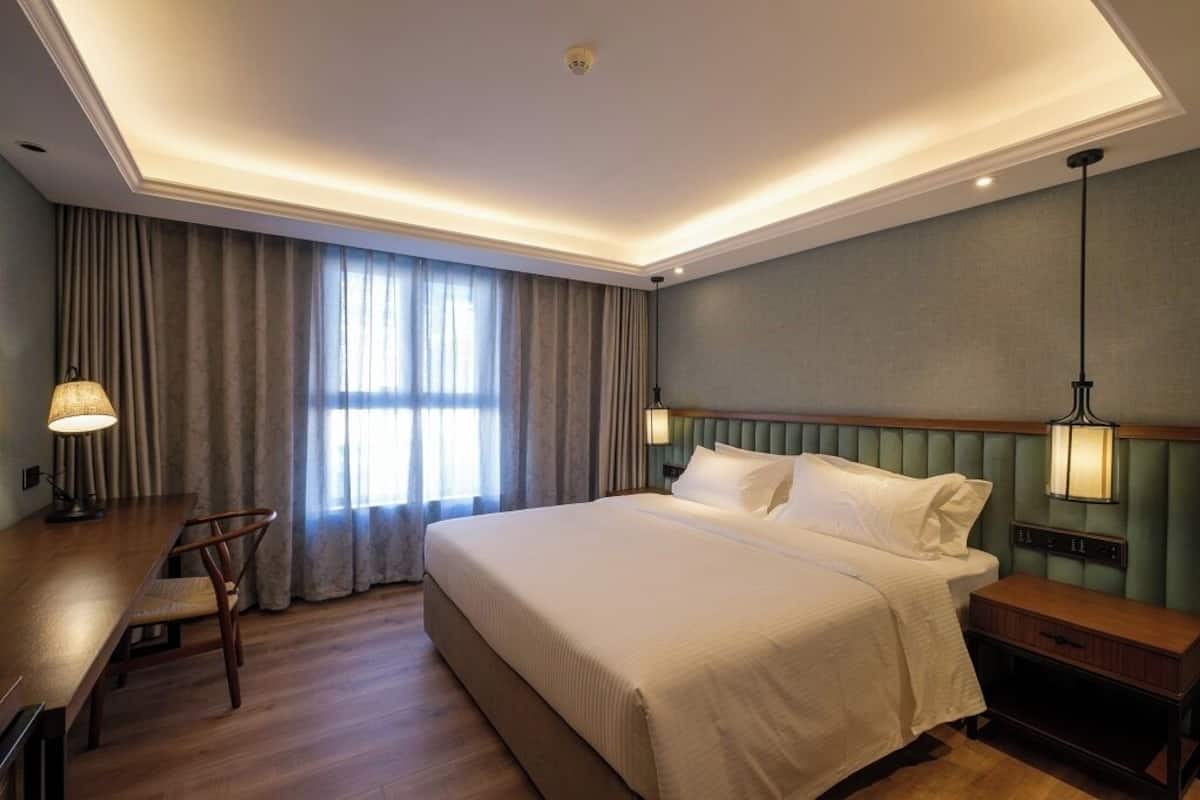 Habitación de hotel con una cama grande, un escritorio con silla, una mesita de noche y una lámpara.