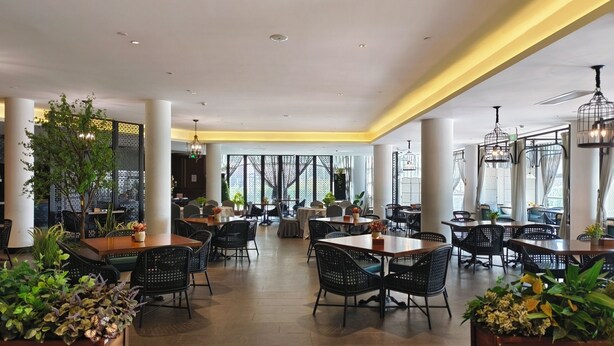 A spacious indoor dining area with multiple tables and chairs, large windows, and decorative plants. - Moon River Puyue Hotel (Tongzhou)