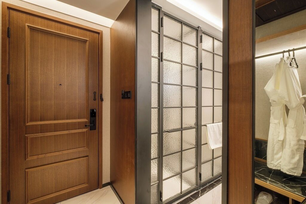 A hotel room with a wooden door, a frosted glass partition, and a clothing rack with white garments.