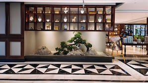 A lobby with a traditional wooden display case containing various decorative items, a bonsai tree, and a patterned floor. - Moon River Puyue Hotel (Tongzhou)