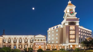 A large hotel with a prominent clock tower, multiple balconies, and well-lit facades. - Moon River Puyue Hotel (Tongzhou)