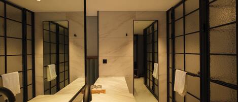 A modern bathroom with a large mirror, a bathtub, and a glass partition.