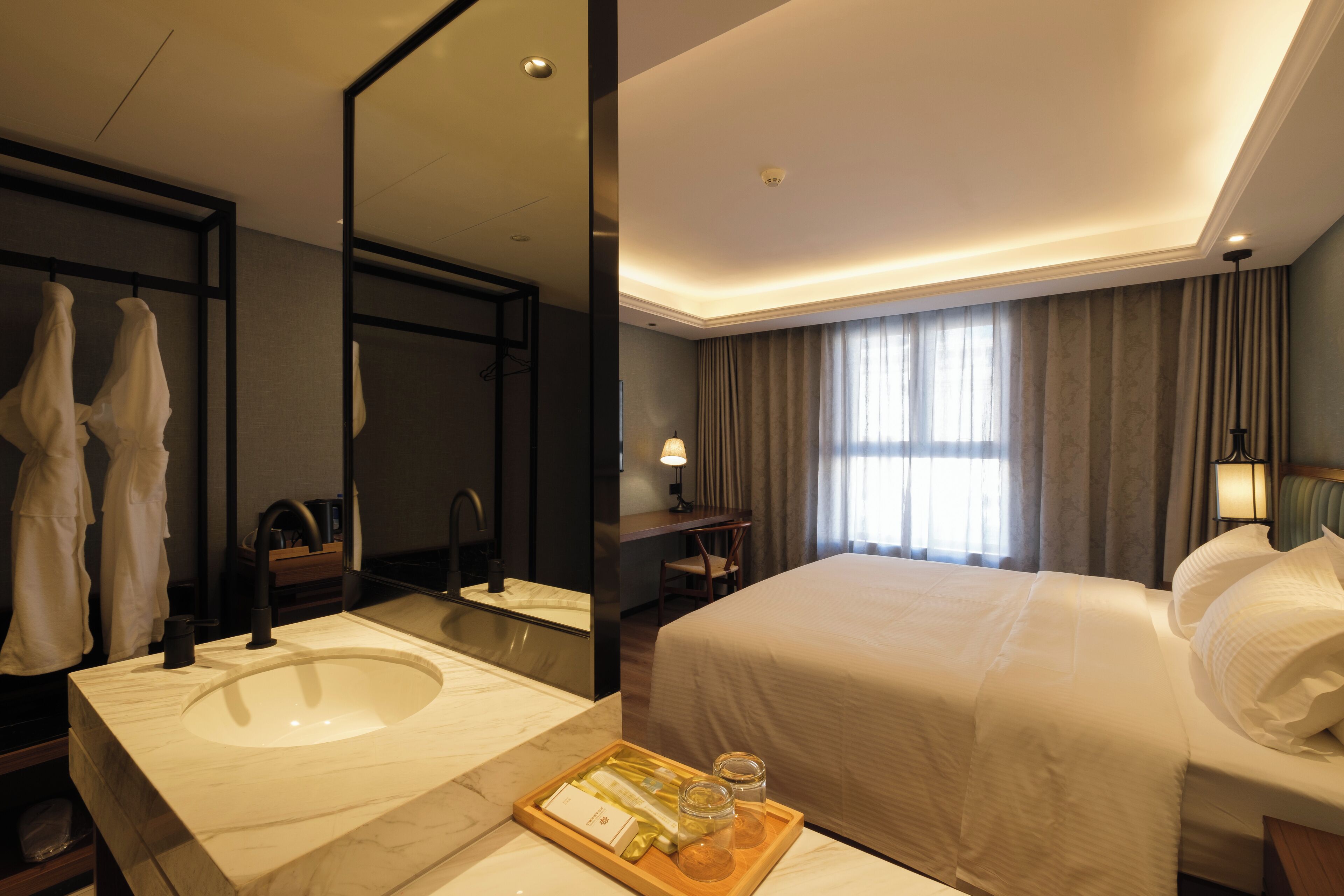 A hotel room with a large bed, a bathroom with a sink and mirror, and a tray with toiletries.