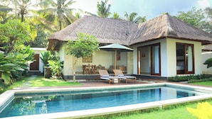 A poolside area with a thatched-roof building, a lounge chair, and a small table. - Luxury Villa Stay – Serenity, Style, and Convenience Combined (Badung)