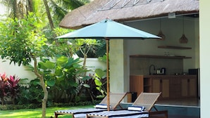 A poolside area with lounge chairs and a thatched-roof structure, surrounded by lush greenery. - Luxury Villa Stay – Serenity, Style, and Convenience Combined (Badung)