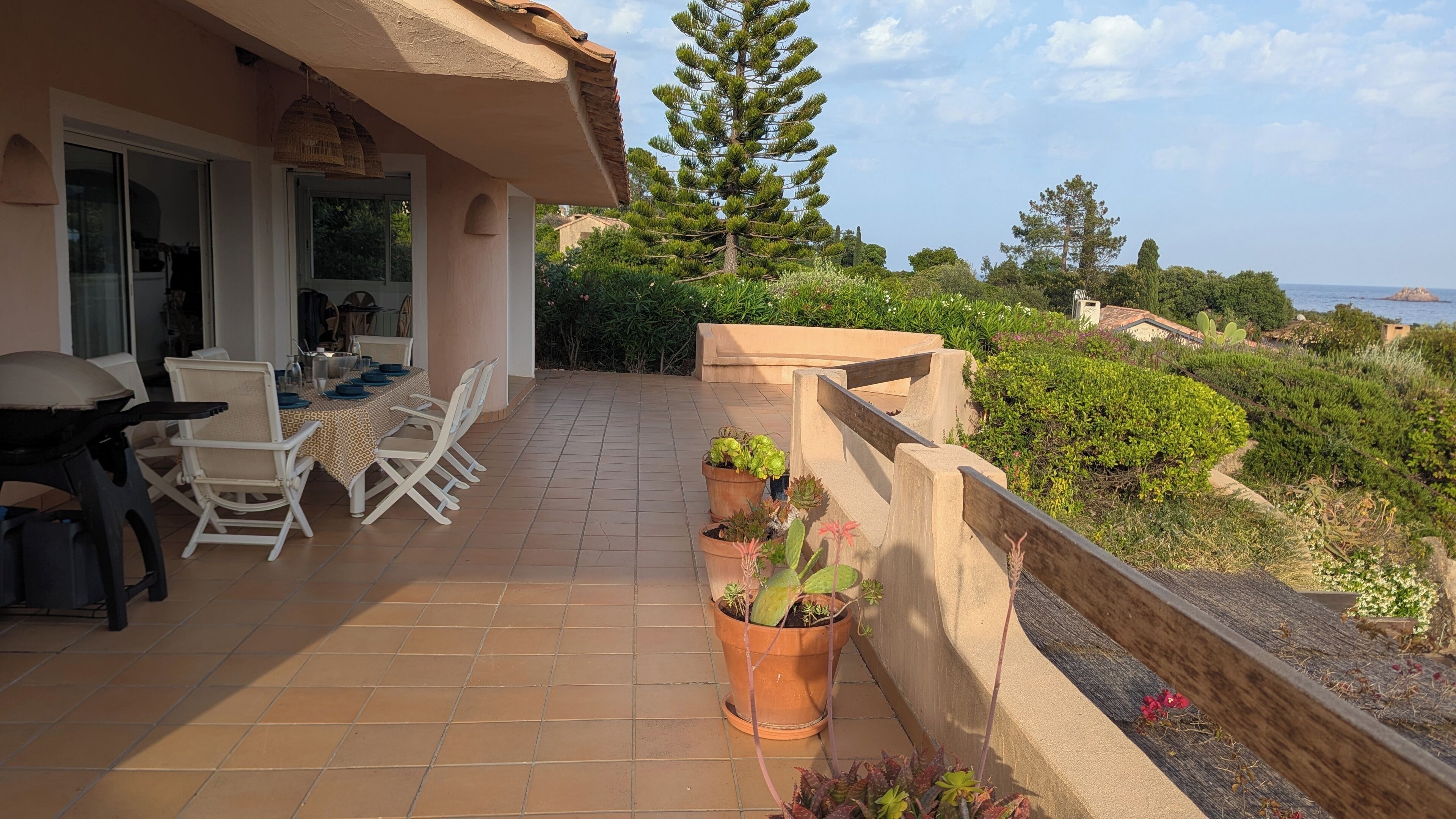 Una terraza con zona de comedor, plantas en macetas y vista al mar.