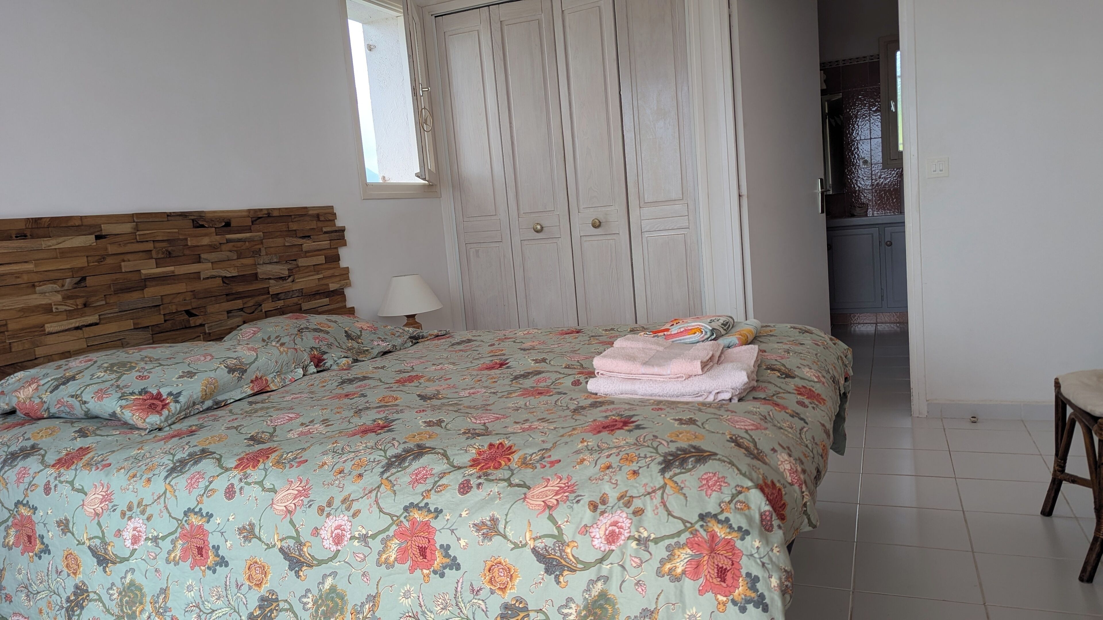 A bedroom with a floral bedspread, a wooden headboard, a bedside lamp, and a wardrobe with multiple doors.