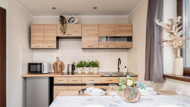 Una cocina moderna con armarios de madera, microondas integrado y un refrigerador pequeño.