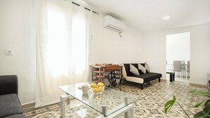 Ein modernes Wohnzimmer mit einem Glastisch, einer Couch, einem Esstisch mit Stühlen und einem gemusterten Boden.