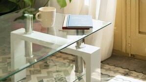 Ein Tisch mit Glasplatte, eine weiße Tasse, ein Buch und eine kleine Flasche.