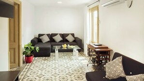 Ein Wohnzimmer mit einem dunkelgrauen Sofa, einem Glastisch und einem gemusterten Boden.