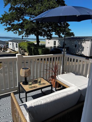 A balcony with a white railing, a wicker chair, a small table with a glass, and an umbrella.