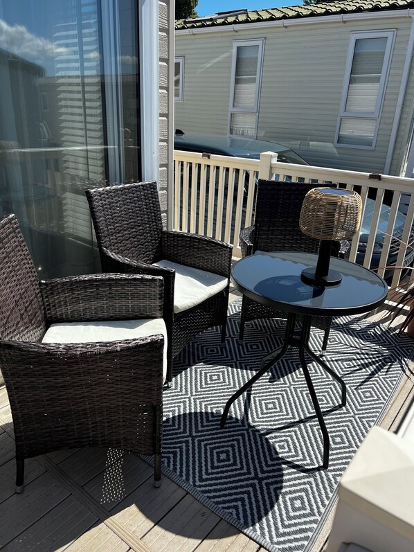 A balcony with wicker chairs and a table, a patterned rug, and a view of a building with windows.