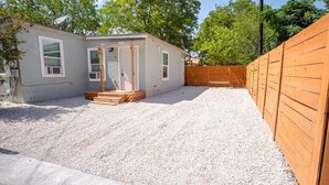 A small, single-story house with a gravel driveway and a wooden fence.