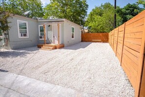 A small, single-story house with a gravel driveway and a wooden fence.