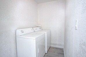 Ein Waschraum mit zwei weißen, frontgeladenen Waschmaschinen und Trocknern, einer weißen, strukturierten Wand und einem Holzboden.