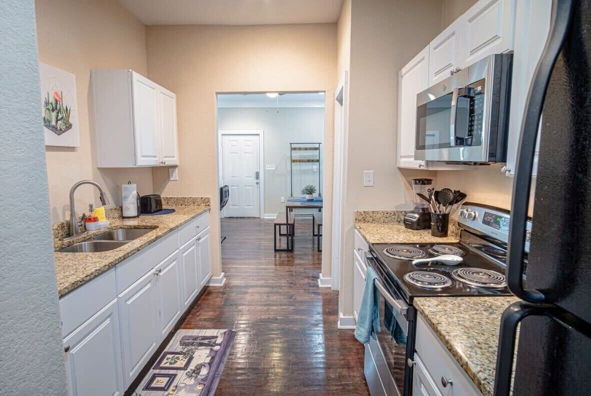 A kitchen with white cabinets, a granite countertop, a stove, and a microwave.