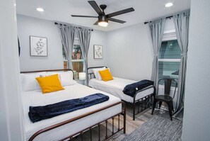 Un dormitorio con dos camas, un ventilador de techo y una ventana con cortinas.