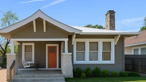 A single-story house with a front porch, a stone chimney, and a well-maintained lawn. - Gorgeous Artistic Fully Fenced Home Near Downtown (San Antonio)