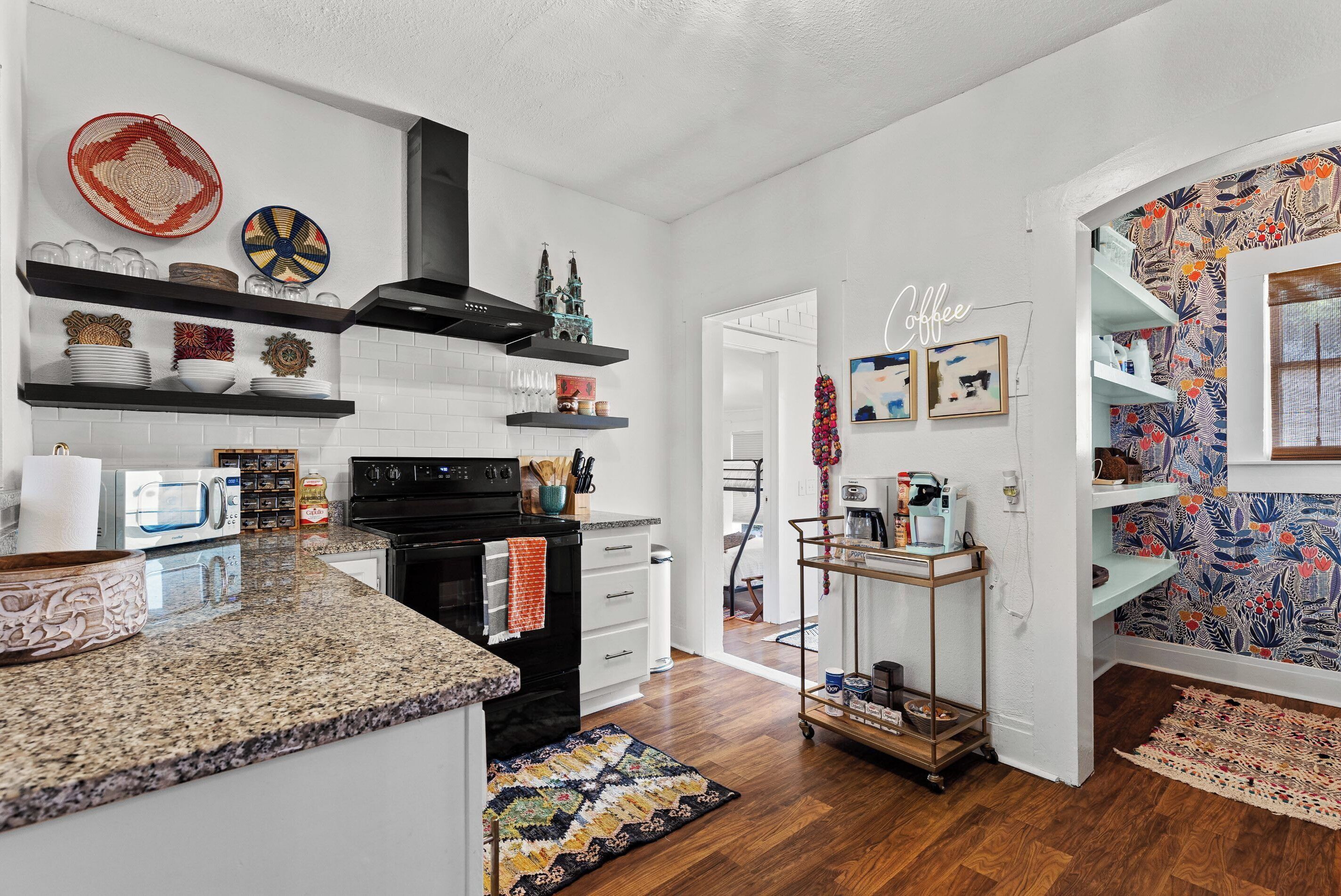 A modern kitchen with white cabinetry, granite countertops, and a black range hood. There are decorative plates and a small model castle on the shelves.