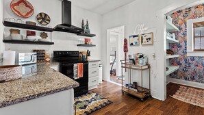 A modern kitchen with white cabinetry, granite countertops, and a black range hood. There are decorative plates and a small model castle on the shelves. - Gorgeous Artistic Fully Fenced Home Near Downtown (San Antonio)