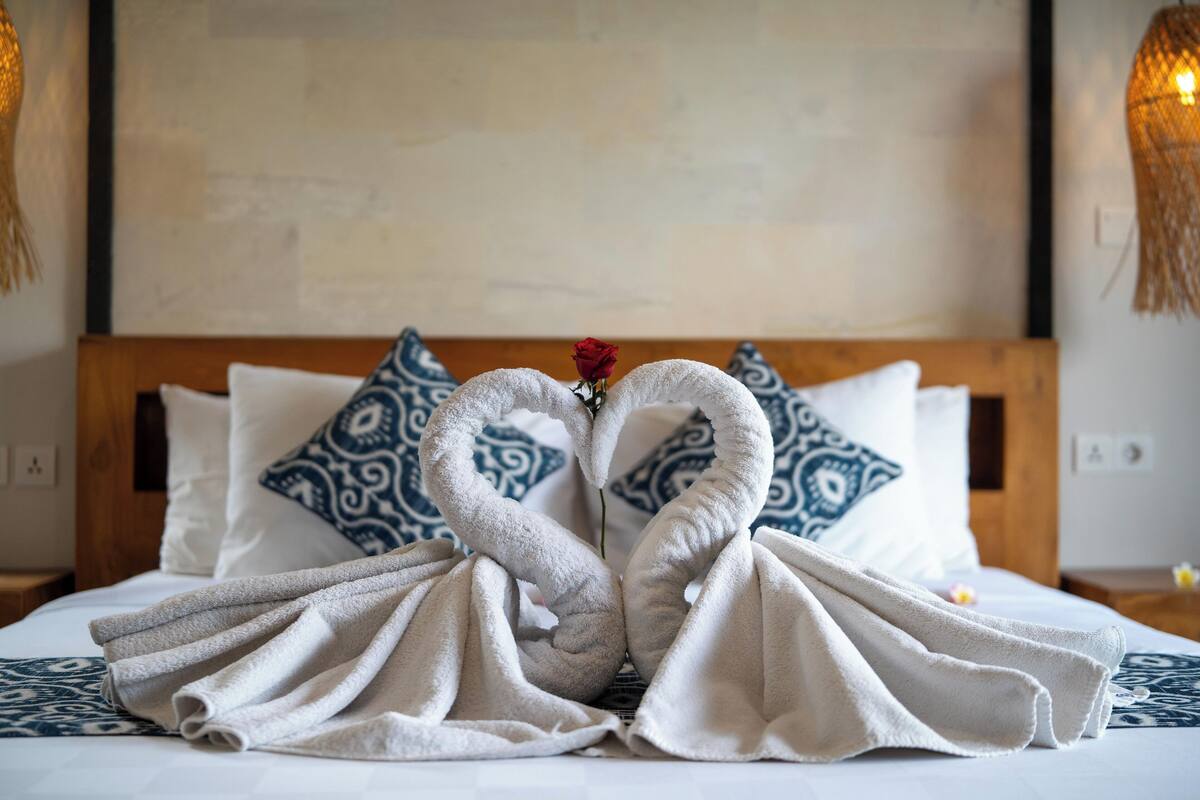 A bed with towels arranged in the shape of two swans, a single rose, and patterned pillows.
