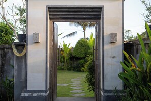A pathway leading to a building entrance with a stone path, surrounded by greenery and a palm tree in the background. - Kesuma Inn Private Villa (Ubud)