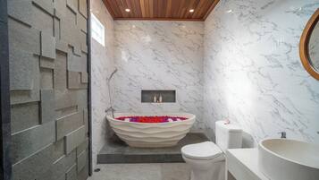 Un baño moderno con una bañera independiente, inodoro y lavamanos.