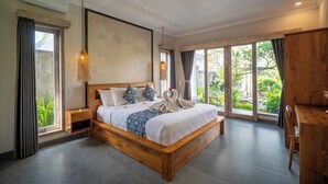 A spacious bedroom with a large bed, wooden headboard, and a view of greenery through large windows. - Kesuma Inn Private Villa (Ubud)