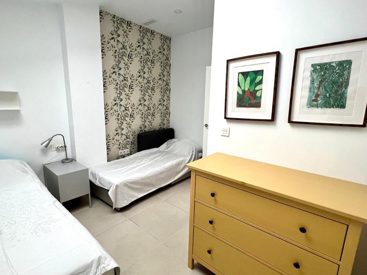Quarto com duas camas de solteiro, mesa de cabeceira com abajur, cômoda e duas quadros decorativos na parede.