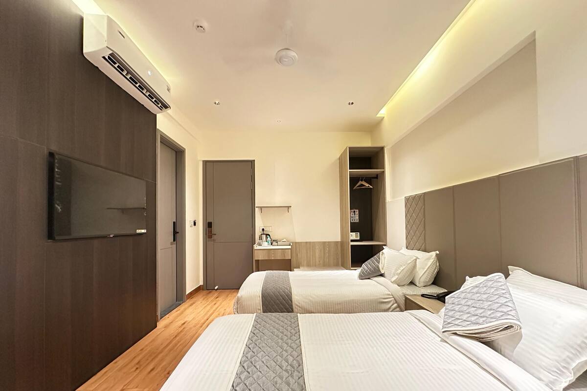 A hotel room with two beds, a TV, a wardrobe, and a bathroom.