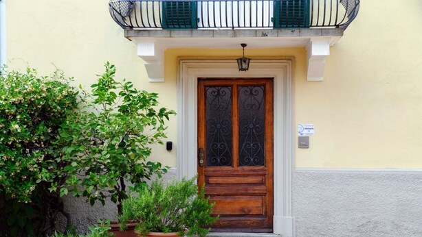 A building with a wooden door, potted plants, and a balcony with green railings. - Close to the Center of Lugano (Sestante 2) (Viganello)