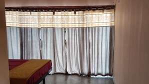 Ein Zimmer mit Bett, Deckenventilator, Klimaanlage und einem Fenster mit Vorhängen.