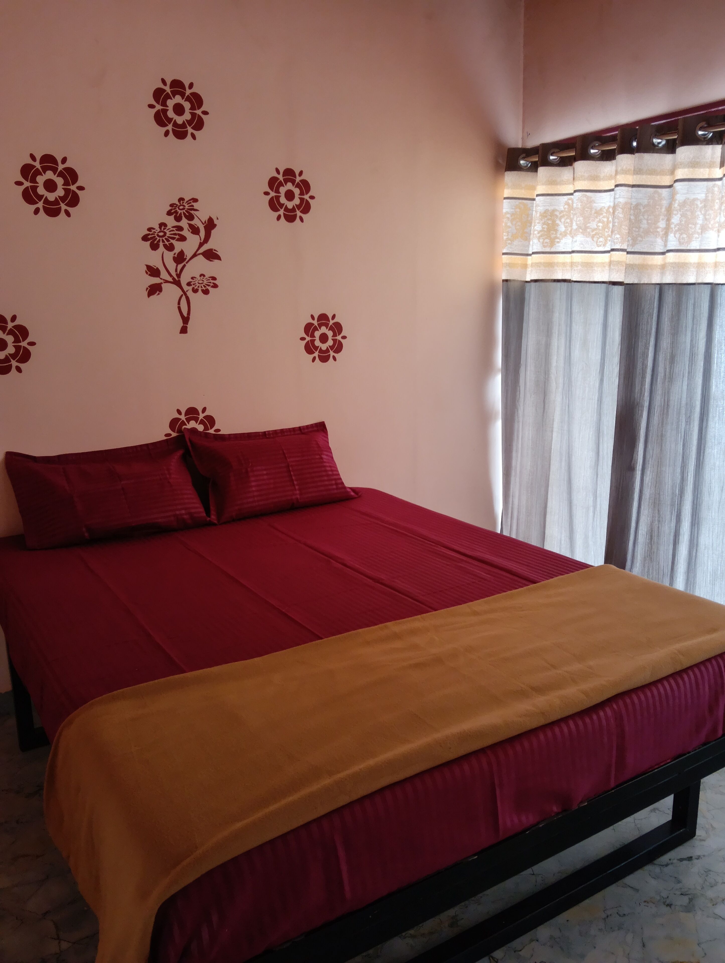 A bed with red and gold bedding, a floral wall decal, and a window with curtains.