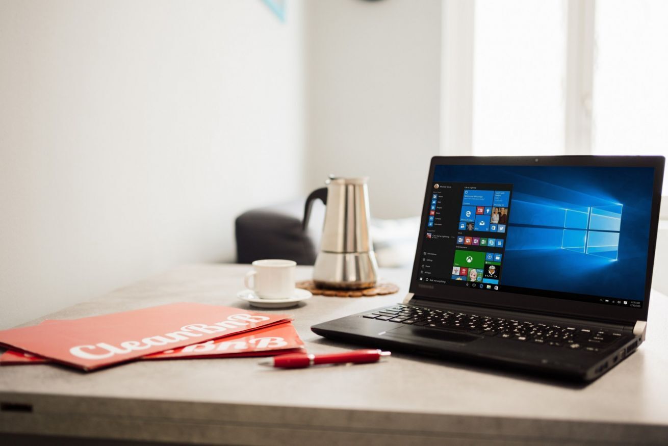 Ein Laptop auf einem Tisch mit einer Tasse und einem roten Notizbuch.