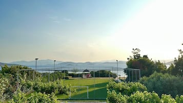 A landscaped garden with a stone fountain, benches, and a view of a sports field and mountains.