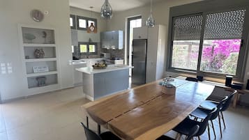 A modern kitchen with a central island, a dining area with a wooden table and black chairs, and a view of vibrant flowers through the window.
