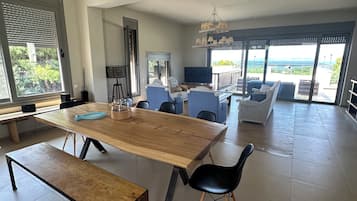 A spacious living area with a large wooden table, multiple chairs, a sofa, and a balcony with a view.