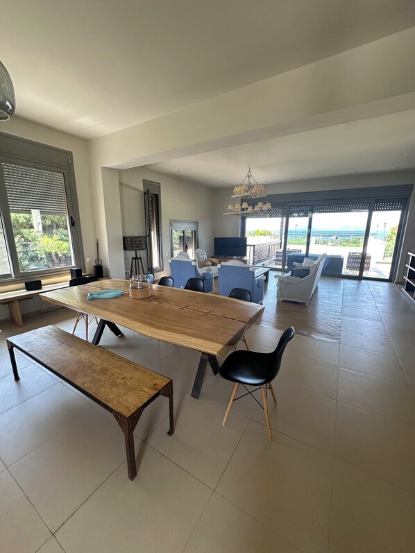 A spacious living area with a large wooden table, multiple chairs, a sofa, and a balcony with a view.